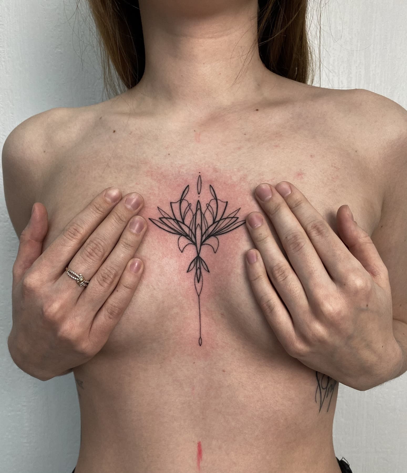 Fine-Line-Lotusblüten-Tattoo am Brustbein