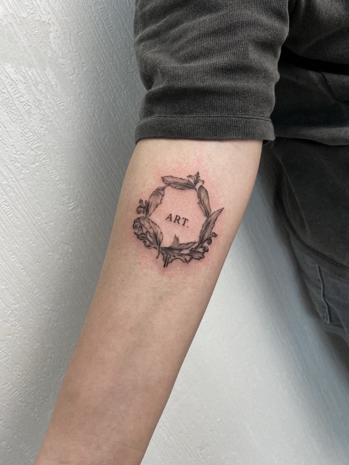 Fine-Line-Schriftzug-Tattoo mit Kranz am Unterarm