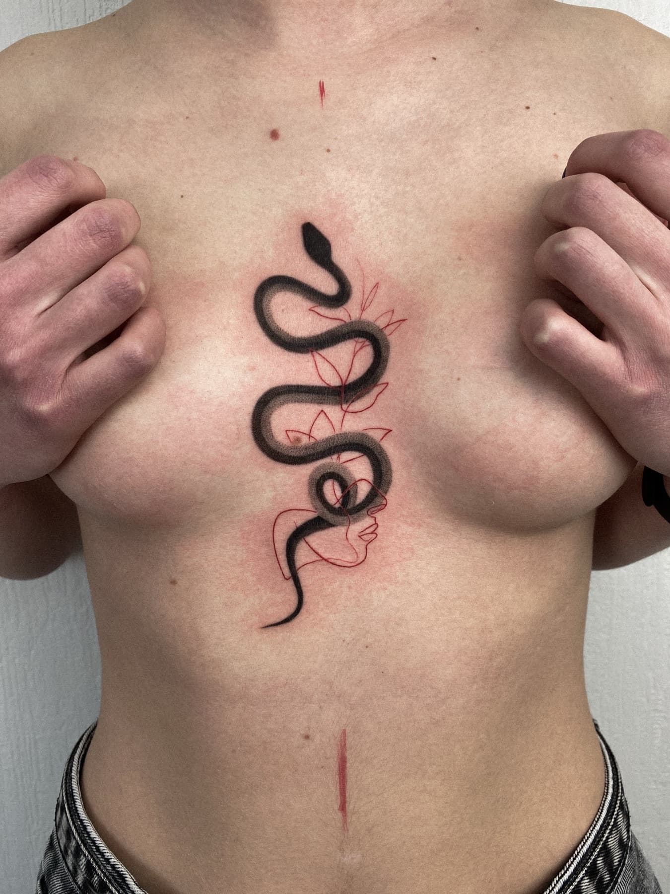 Fine-Line-Schlangen-Tattoo mit Zweig am Brustbein