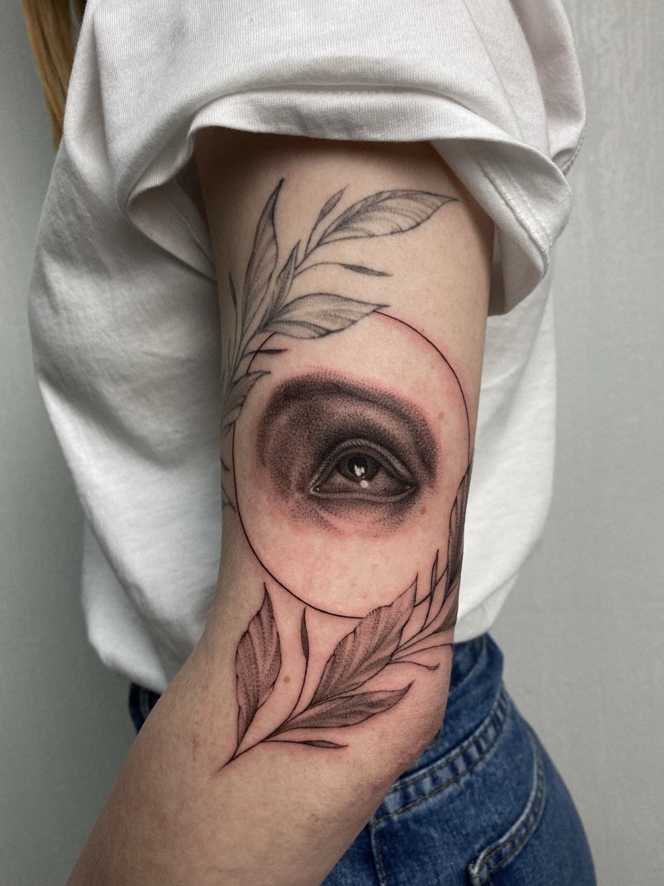 Micro-Realism-Augen-Tattoo mit Fine-Line-Blättern am Oberarm