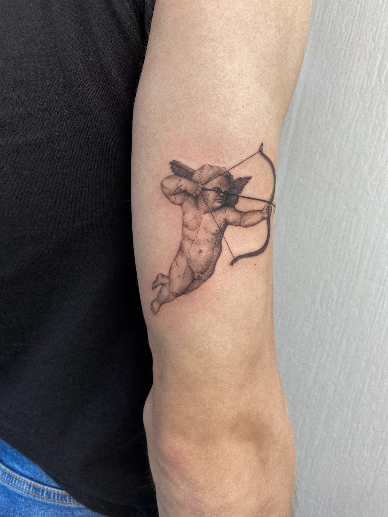 Illustratives Amor-Tattoo am Oberarm